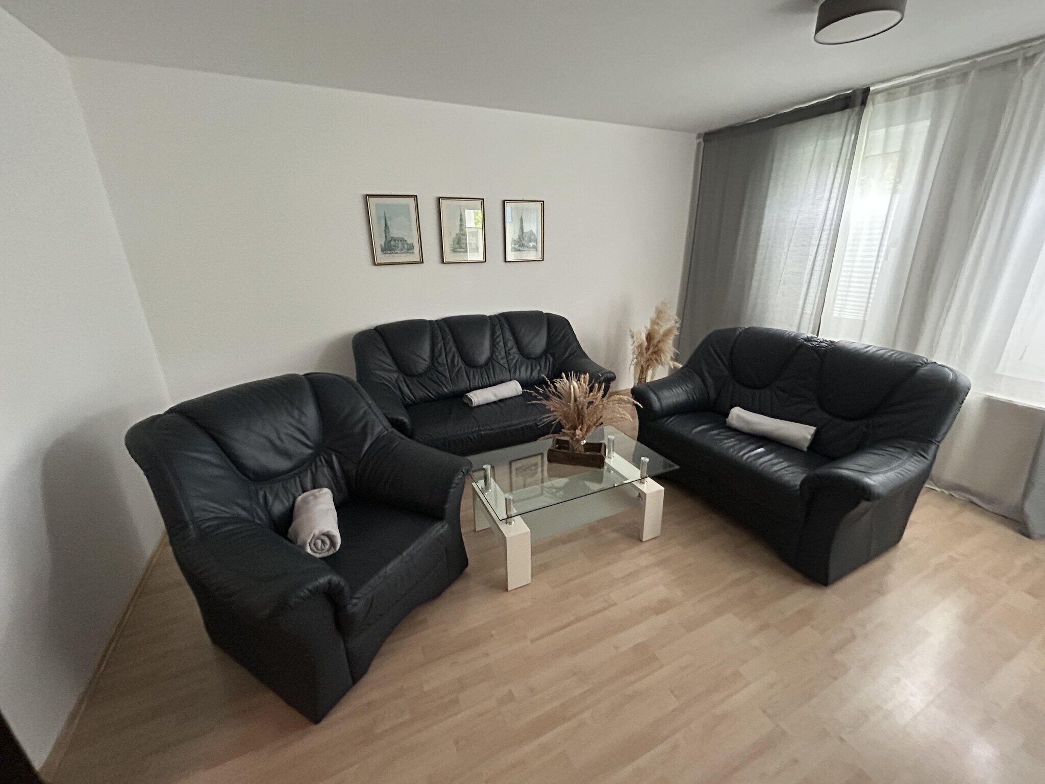 A modern living room with two black leather sofas, a glass coffee table, and three framed pictures on the wall.