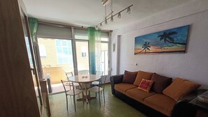 Un soggiorno con un divano marrone, un tavolo da pranzo con sedie e un quadro raffigurante un tramonto.