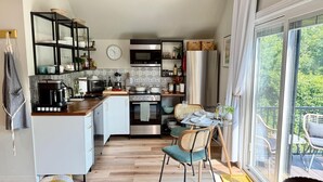 A modern kitchen with a dining area, a large window, and a view of greenery.