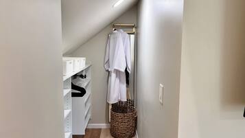 A narrow hallway with a white shelving unit, a hanging rack with clothes, and a wicker basket.