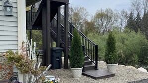 A residential building with a dark staircase leading to a balcony, surrounded by potted plants and gravel.