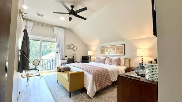 A bedroom with a bed, a desk, a chair, a sofa, a ceiling fan, and a view of the outdoors.