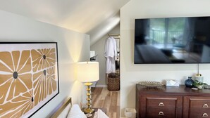 A bedroom with a bed, a bedside lamp, a TV mounted on the wall, and a wooden dresser.