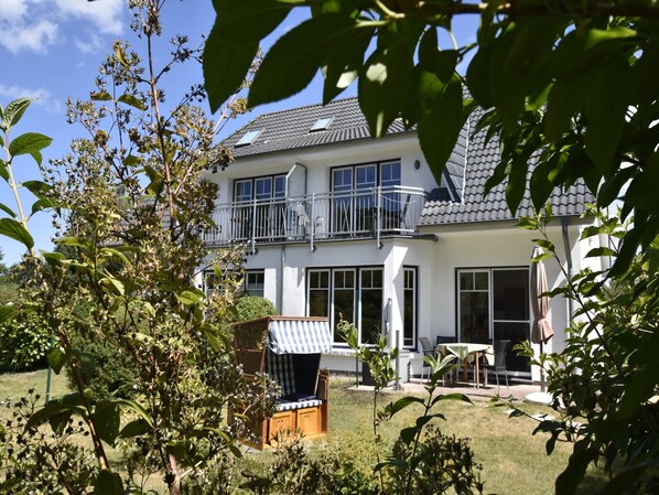 A two-story house with a balcony, a covered outdoor seating area, and a lawn.