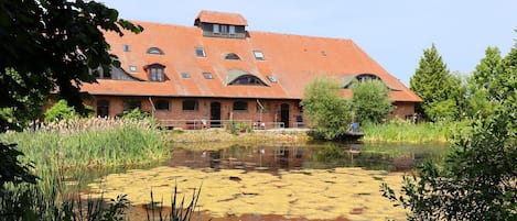 A large brick building with a red-tiled roof, surrounded by a pond and greenery.