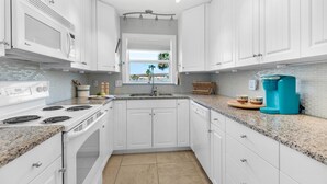 A modern kitchen with white cabinets, a granite countertop, a built-in microwave, and a coffee maker.
