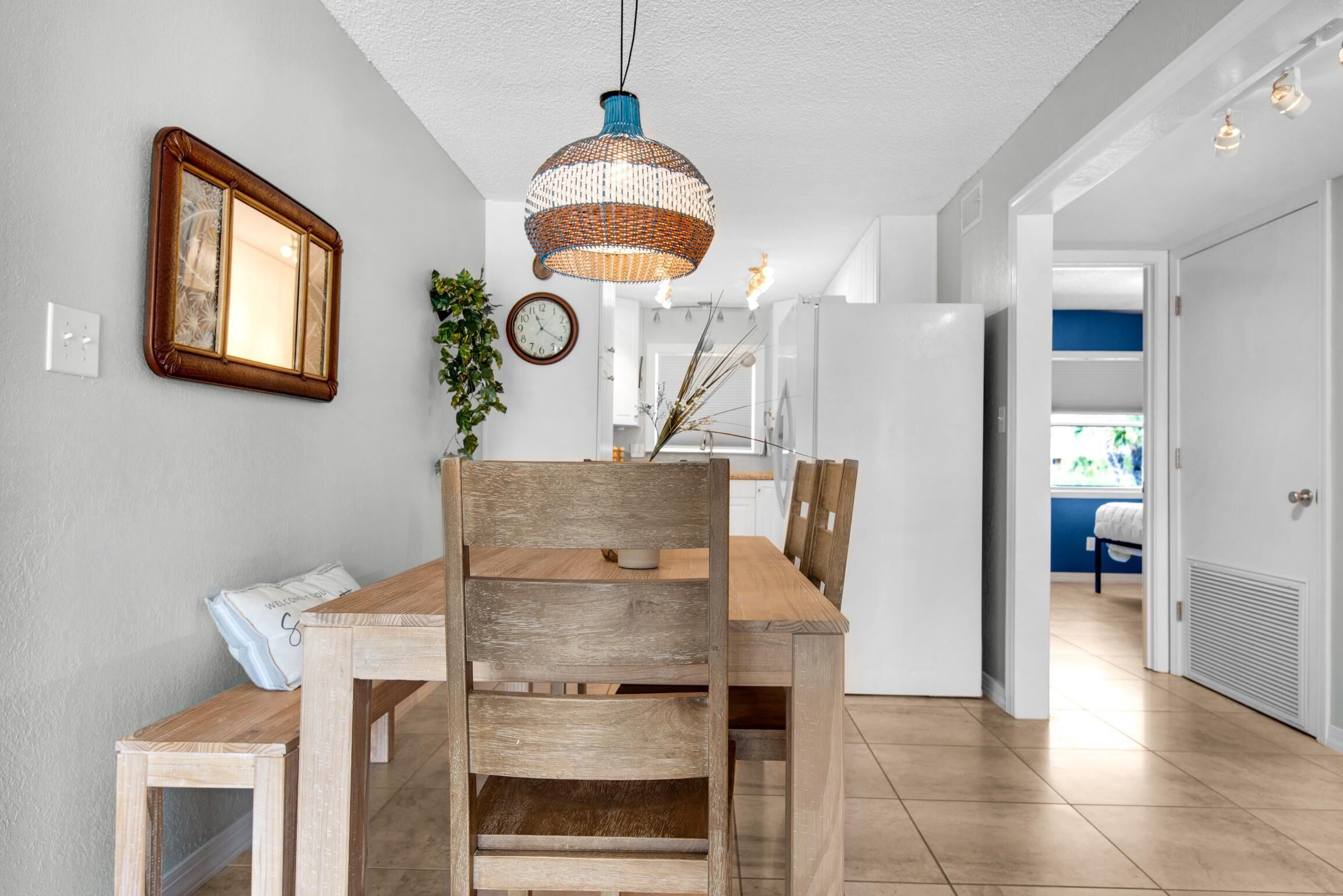 A dining area with a wooden table and chairs, a hanging light fixture, a wall clock, and a framed picture.