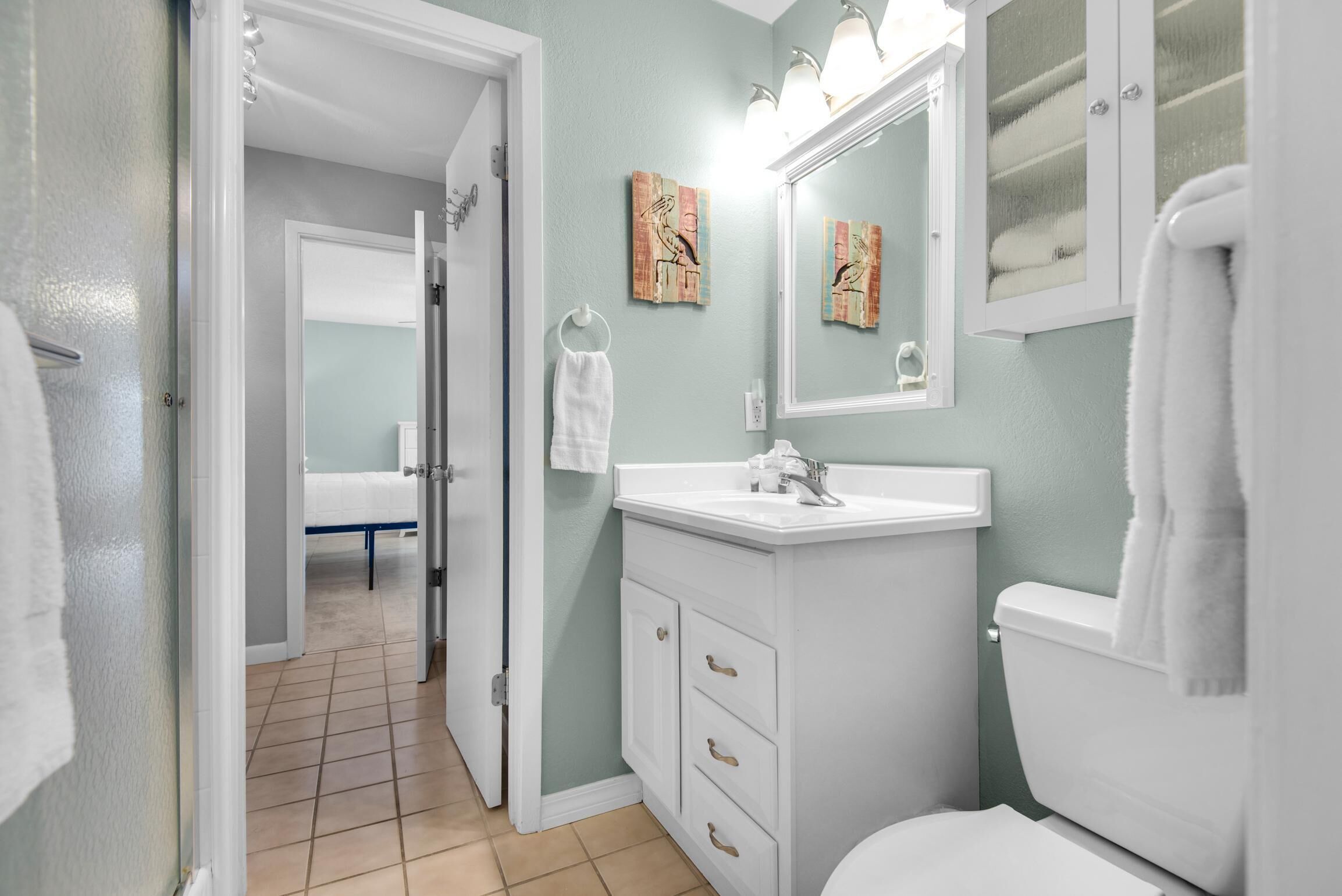 A bathroom with a white sink, mirror, and toilet. There is a towel rack and a door leading to another room.