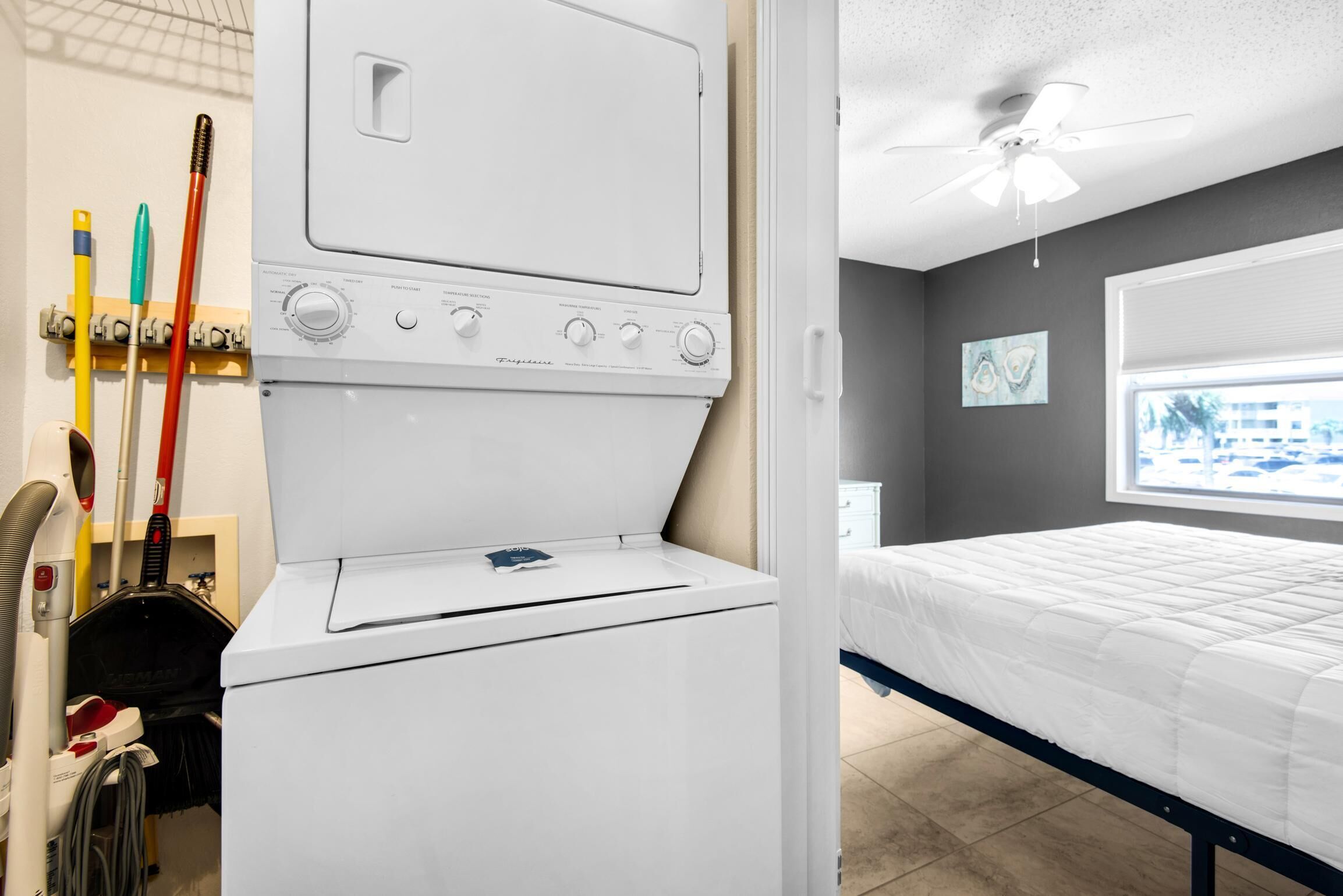 A laundry area with a white washer and dryer, a ceiling fan, and a bed with a white mattress.