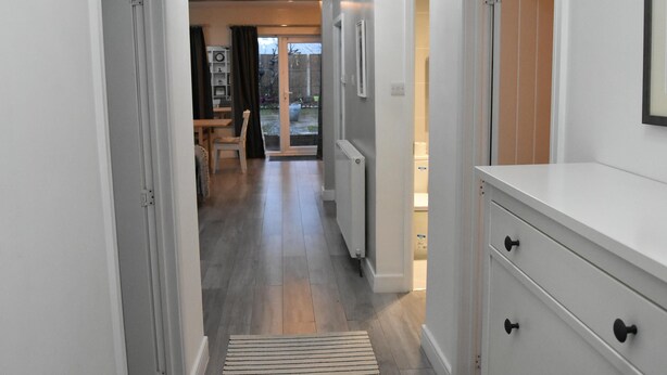 A hallway with a radiator, a wooden floor, and a door leading to a room with a window. - Charming Wembley Home Near Wembley Stadium (Wembley)