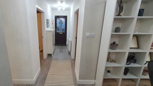 A narrow hallway with a striped rug, white walls, and a white shelving unit with decorative items. - Charming Wembley Home Near Wembley Stadium (Wembley)