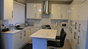 A modern kitchen with white cabinets, a marble countertop, a stainless steel range hood, and a black chair. - Charming Wembley Home Near Wembley Stadium (Wembley)