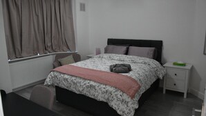 A bedroom with a bed, a nightstand, a chair, and a window with curtains. - Charming Wembley Home Near Wembley Stadium (Wembley)