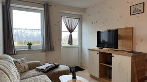 Ein gemütliches Wohnzimmer mit einer Couch, einem kleinen Tisch, einem Fernseher auf einem Holzboden und einem Bücherregal.