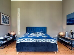 Een slaapkamer met een groot bed, een boekenplank, een nachtkastje en een schilderij aan de muur.