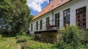 Une maison à deux étages dotée d’un balcon, entourée d’une végétation luxuriante et d’une pelouse bien entretenue.