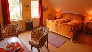 A cozy bedroom with a wooden bed, two chairs, a desk, and a window with red curtains. - Moderne Ferienwohnung im Schwedenhaus (Wittenbeck)