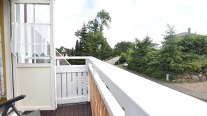 A balcony with a wooden floor, white railing, and a view of a residential area with trees and houses. - Moderne Ferienwohnung im Schwedenhaus (Wittenbeck)