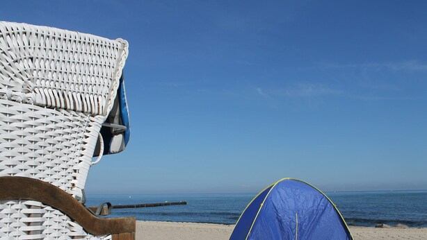 A beach scene with a white wicker chair and a blue tent on the sand. - Moderne Ferienwohnung im Schwedenhaus (Wittenbeck)