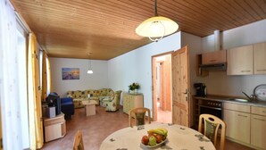 A cozy room with a wooden ceiling, a dining table with a fruit bowl, a sofa, and a kitchen area with wooden cabinets. - Ferienhaus in Damshagen mit Sauna (Klütz)