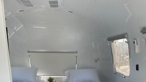 Un intérieur de camping-car compact comprenant deux lits, une petite kitchenette et une fenêtre offrant une vue sur l’extérieur.