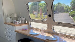 Une petite cuisine équipée avec une fenêtre donnant sur l’extérieur, une machine à café, des tasses et une poubelle.