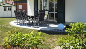 Une terrasse extérieure avec une table et des chaises, deux parasols jaunes et, au fond, un bâtiment doté d’un toit de chaume.