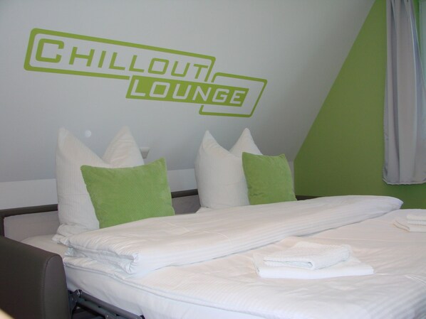 A hotel room with a bed, pillows, and a wall sign that reads "Chillout Lounge".