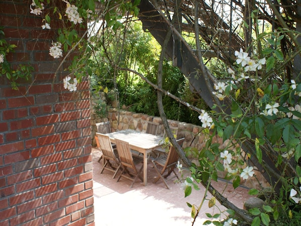 An outdoor patio with a brick wall, a wooden table, and chairs.