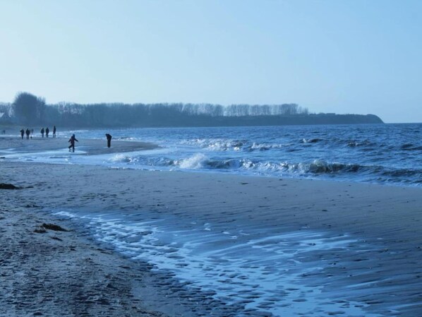 A beach with people walking along the shore.