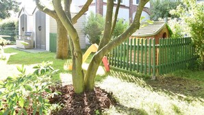 A tree with a swing set and a small playhouse behind a green fence. - Romantische Ferienwohnung in Boldenshagen (Kröpelin OT Boldenshagen)