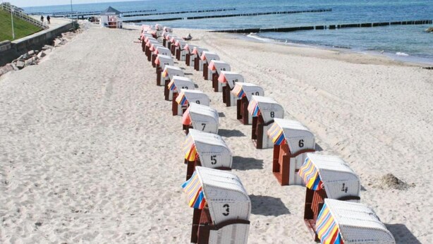 A beach with rows of numbered beach huts along the shore. - Romantische Ferienwohnung in Boldenshagen (Kröpelin OT Boldenshagen)