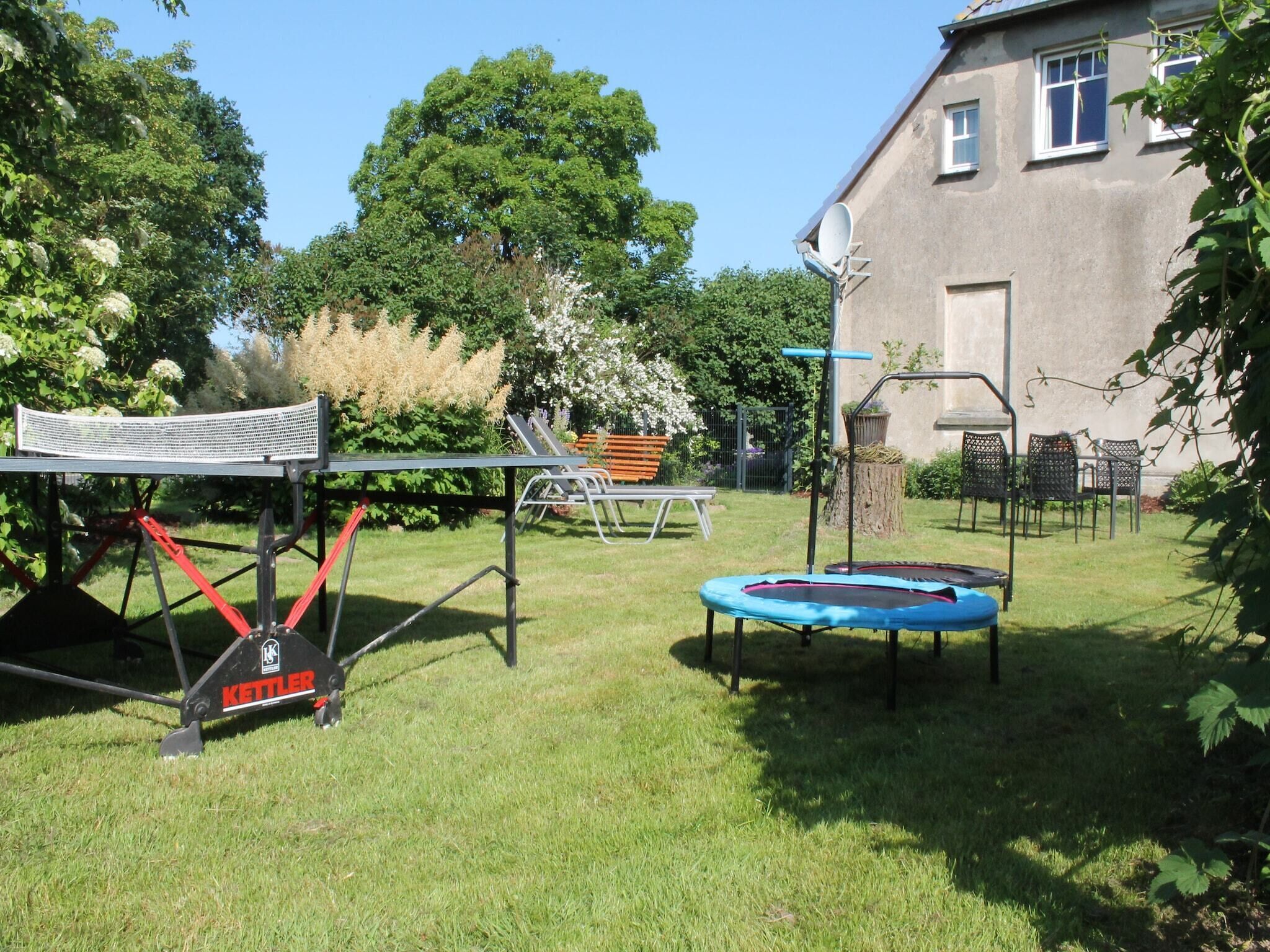 Un patio trasero con una red de bádminton, un trampolín y mobiliario de exterior.