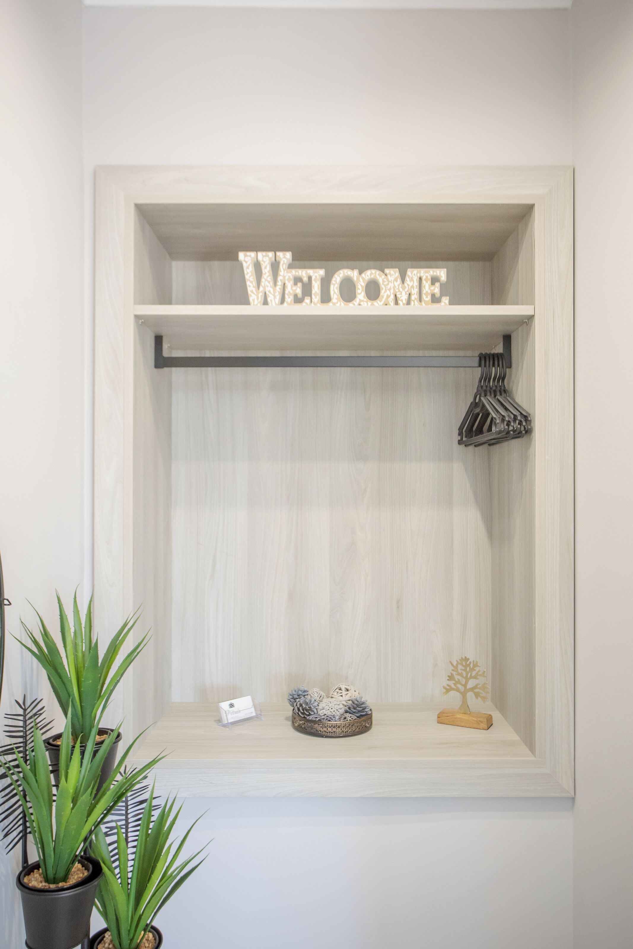 Un estante de madera con un letrero que dice 'WELCOME', una planta pequeña, un adorno y un perchero.
