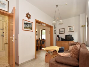 A living room with a brown sofa, a wooden coffee table, and a television. There are framed pictures on the wall and a door leading to another room.