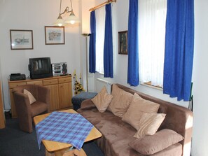 En stue med sofa, fjernsyn, et bord med ternet dug og blå gardiner.