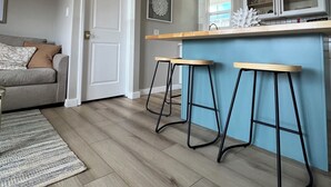 Eine moderne Küche mit Holzbalkendecke, einer Bar mit Hockern und einem Essbereich mit Sofa und Teppich.