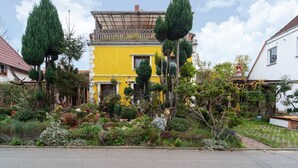 A yellow building with a balcony, surrounded by various plants and trees. - Ferienwohnung mit Wintergarten in Wismar (Wismar)