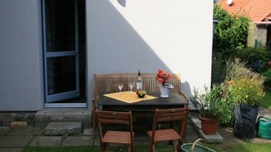 An outdoor patio with a table, chairs, and a bench. There is a potted plant and a basket on the ground.