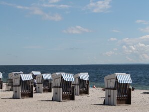 Strandstolar med randiga soltak placerade på en sandstrand, vända mot havet.