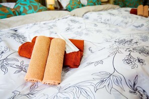 A bed with floral-patterned bedding, two rolled towels, and a white tissue.