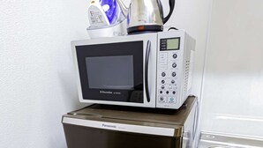 A compact kitchenette with a microwave, kettle, and coffee maker on top of a refrigerator.