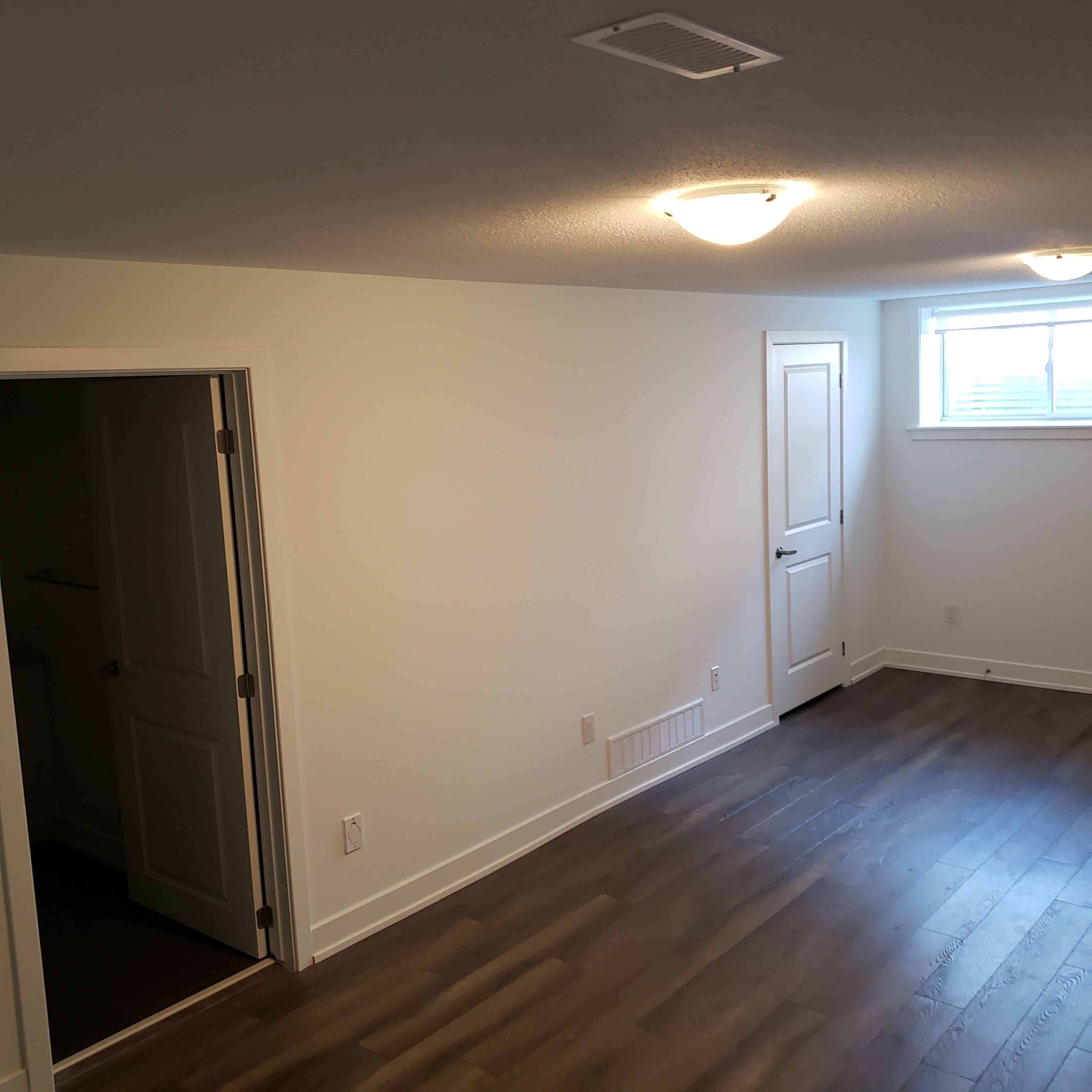 Ein geräumiges Zimmer mit Holzdielenboden, weißen Wänden und einer Tür zu einem anderen Raum.