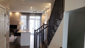 Eine moderne Küche mit einer zentralen Kochinsel, einem Essbereich mit Stühlen und einer Treppe mit Geländer.