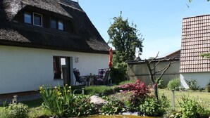 Une maison à toit de chaume, avec un jardin, un étang et une table entourée de chaises à l’extérieur.