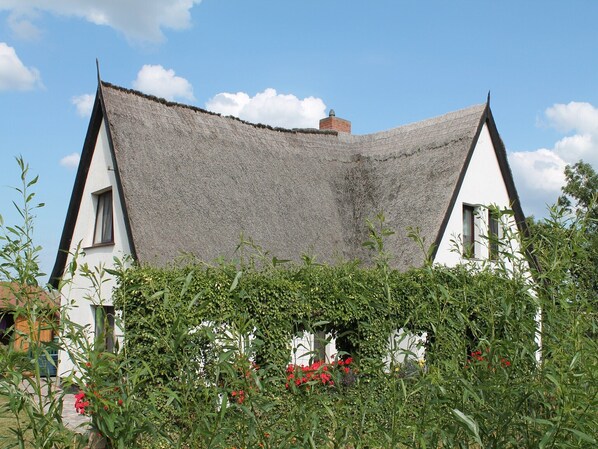 A traditional house with a steeply pitched roof, surrounded by lush greenery and flowering plants.
