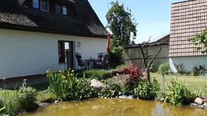 A traditional house with a thatched roof, a small garden with a pond, and a red umbrella. - Ferienwohnung in Pepelow nahe der Ostsee (Pepelow)