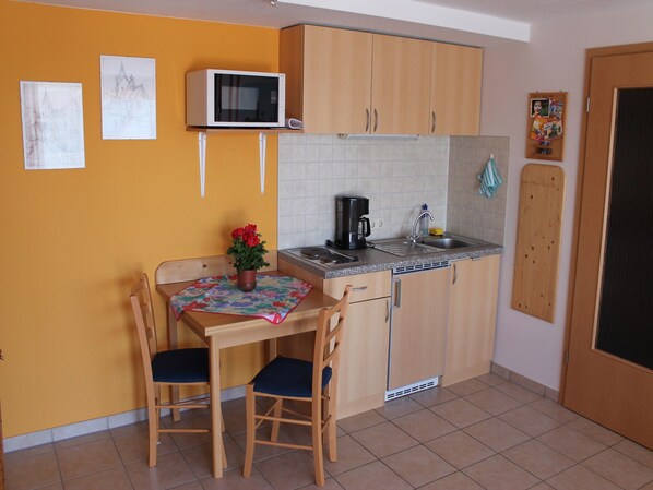 A compact kitchen with a dining table, chairs, a microwave, a coffee maker, and a sink.