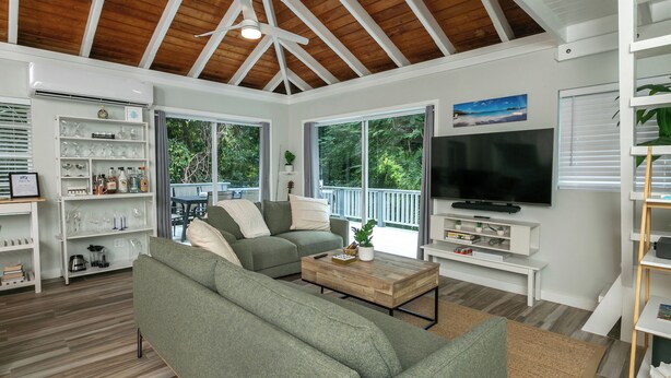 A living room with a wooden ceiling, a green sofa, a coffee table, and a TV. - Villa de Paz, STJ 4 BR/2.5B, 2-8 guests Pool Private Renovated AC backup power (St John)