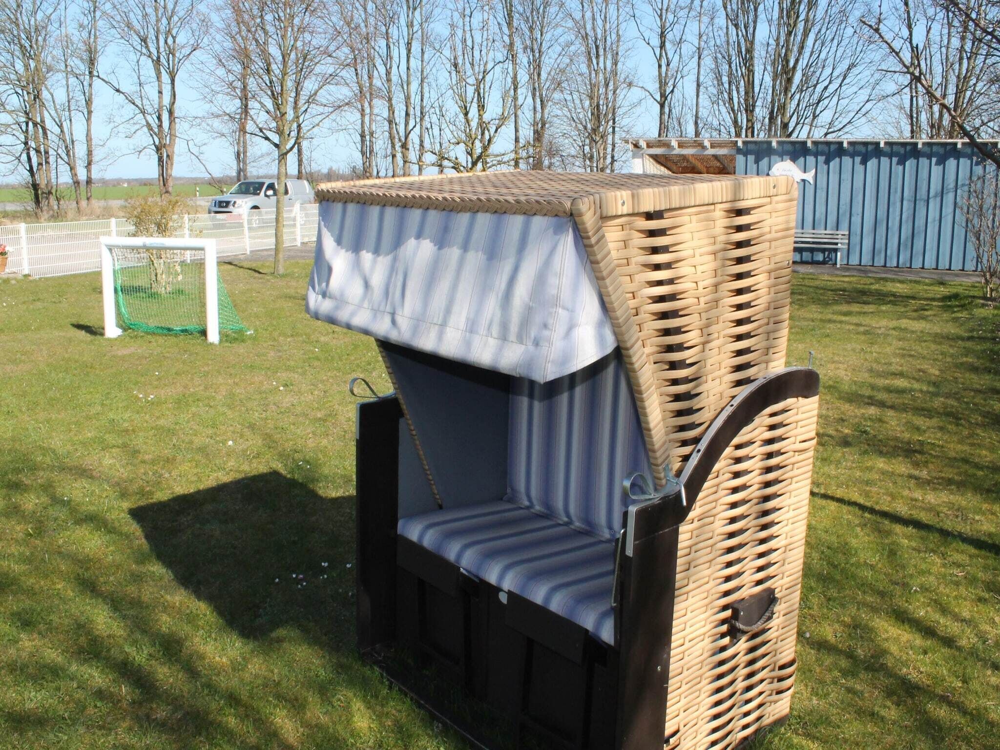 A wicker outdoor seating area with a bench and a table, surrounded by a grassy field and trees.